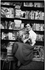 Young woman reading a magazine at a news stand